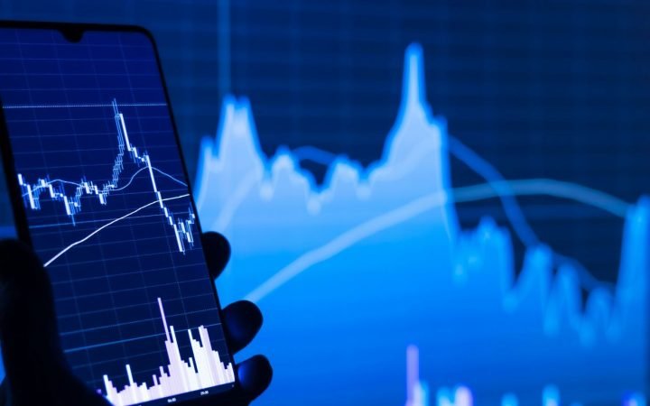 a person holding a cell phone in front of a stock chart