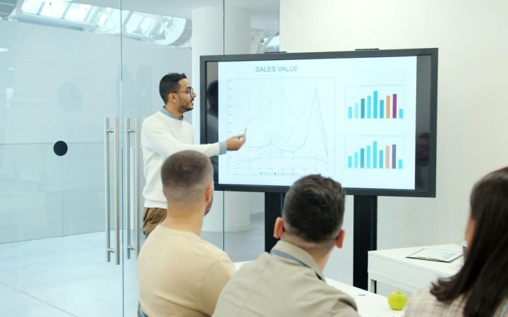 Man presenting charts on a large screen to audience.